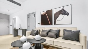 En moderne stue med en beige sofa, dekorative vaser i sort og hvidt, og to billeder af heste i rammer på væggen.
