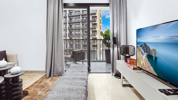 En moderne stue med et stort fladskærms-tv, en sofa, et sofabord og udsigt til en balkon med bybelysning.