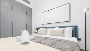 Et moderne soveværelse med en stor seng, en grå garderobe og et sengebord med en lampe.
