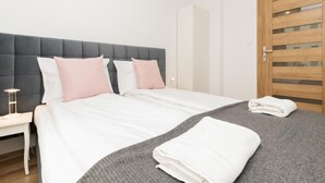 A neatly made bed with white and pink pillows, a grey blanket, and a folded white towel on a grey bedspread.