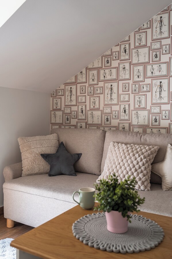 A cozy living room with a beige sofa, a coffee table with a plant, and a wall decorated with framed sketches. - Apartament KOLEJOVA 21 - blisko centrum (Nowy Targ)