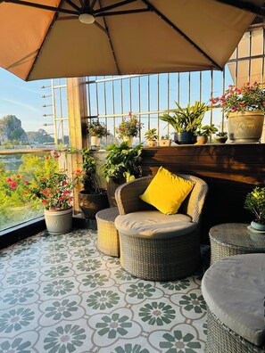 A balcony with wicker furniture, potted plants, and a view of the landscape. - Li River Resort Villa Hotel (Guilin)