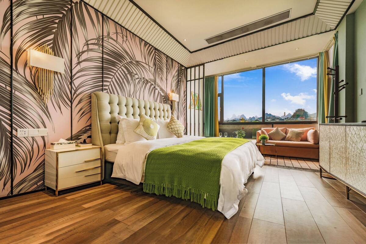 Un dormitorio moderno con una cama grande, una mesita de noche, un plaid verde y vistas al exterior a través de amplias ventanas.