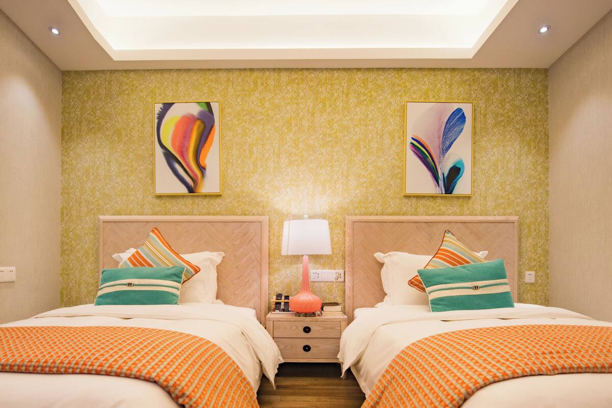 Una habitación de hotel con dos camas, una mesita de noche con lámpara y obras de arte en las paredes.