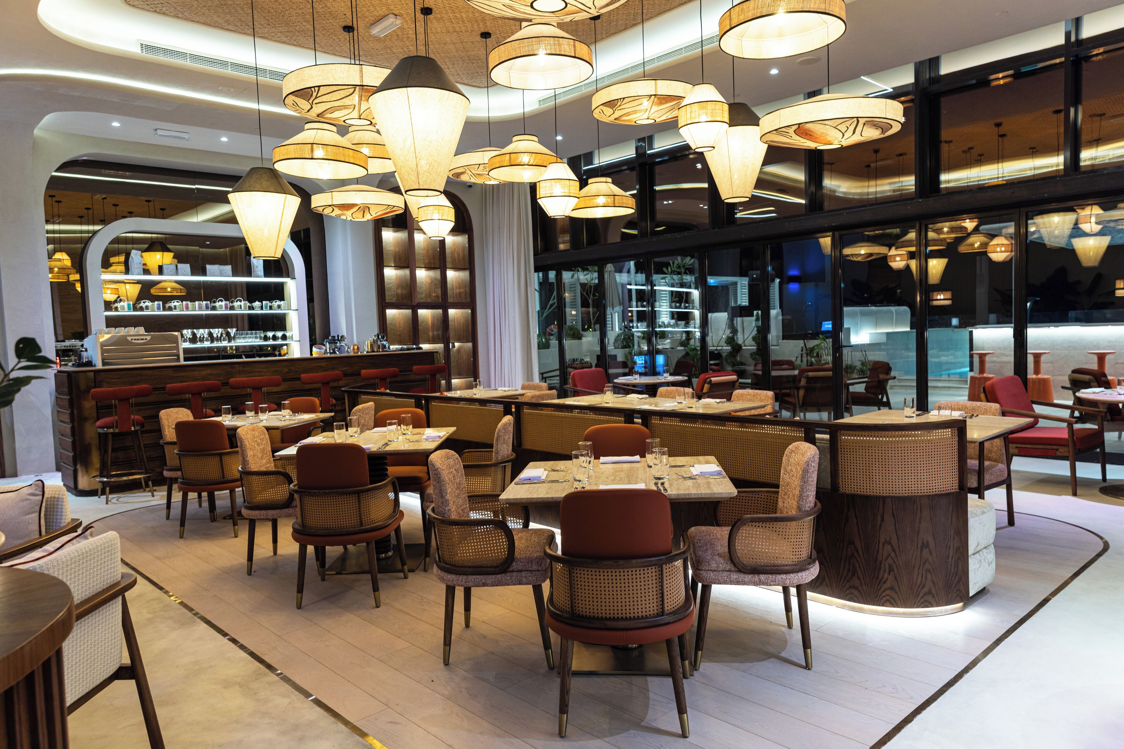 Un intérieur de restaurant moderne, avec plusieurs tables et chaises, un éclairage d’ambiance et un espace bar.