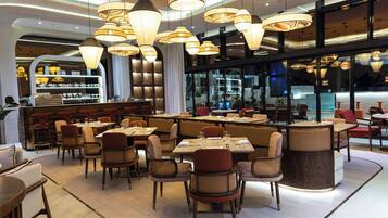 Un intérieur de restaurant moderne, avec plusieurs tables et chaises, un éclairage d’ambiance et un espace bar.