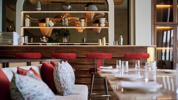 A modern restaurant interior with a bar area, red upholstered stools, and a variety of table settings.