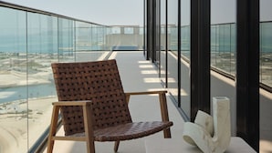 A modern balcony with a glass railing, a woven chair, and a marble table. - The OQ (Lusail)