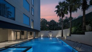 A modern indoor swimming pool with clear water, surrounded by a building with large windows and palm trees. - Welcomhotel By ITC Hotels Delhi-Gurugram Highway (Gurugram)