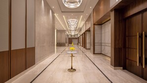 A modern hotel corridor with a marble floor, a central round table with a gold base, and a large circular chandelier. - Welcomhotel By ITC Hotels Delhi-Gurugram Highway (Gurugram)