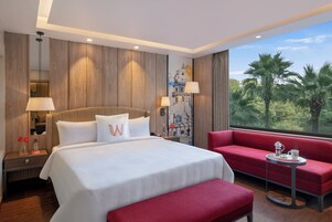 Habitación de hotel con una cama grande, un sofá rojo, una mesita y vistas a palmeras.
