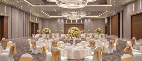 A banquet hall with round tables, white chairs with gold sashes, and large floral centerpieces.