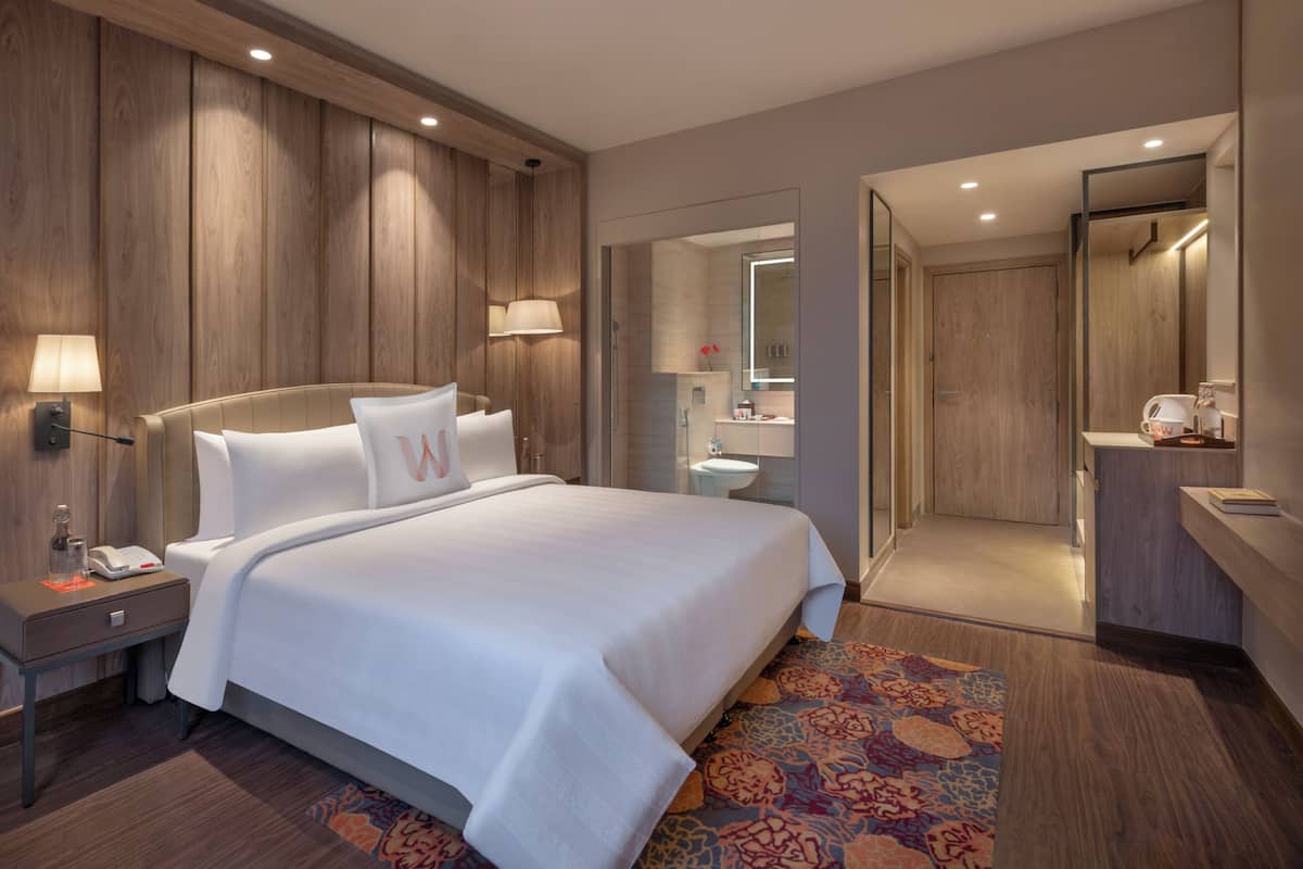 A hotel room with a large bed, bedside lamps, a nightstand, a bathroom with a mirror, sink, and towel rack.