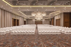 A conference room with rows of white chairs, a patterned carpet, and a large chandelier.