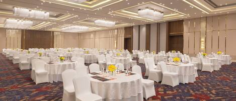 Un amplio salón de banquetes con mesas redondas, sillas blancas y centros de mesa florales.