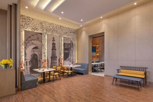 A modern hotel lobby with a wooden floor, seating areas, and a wall with cityscape artwork.