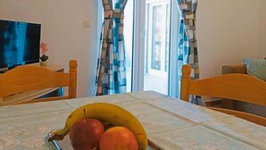 A dining table with a tray of fruit, a television, and curtains in a room.