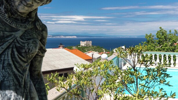 A statue, a swimming pool, and a view of the sea and distant buildings.