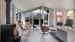 Un salon moderne doté d’un poêle à bois, de sièges confortables, de grandes fenêtres et offrant une vue sur l’extérieur.