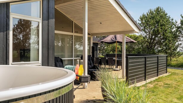Un espace extérieur aménagé avec un patio, un jacuzzi, des sièges et une partie couverte avec un parasol.