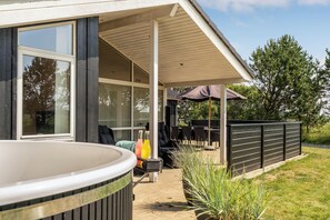 Un espace extérieur aménagé avec un patio, un jacuzzi, des sièges et une partie couverte avec un parasol.