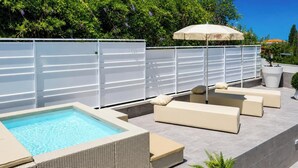 A pool area with a rectangular pool, white lounge chairs, and a pergola with an umbrella. - Hotiday Apartments Cefalù (Cefalù)