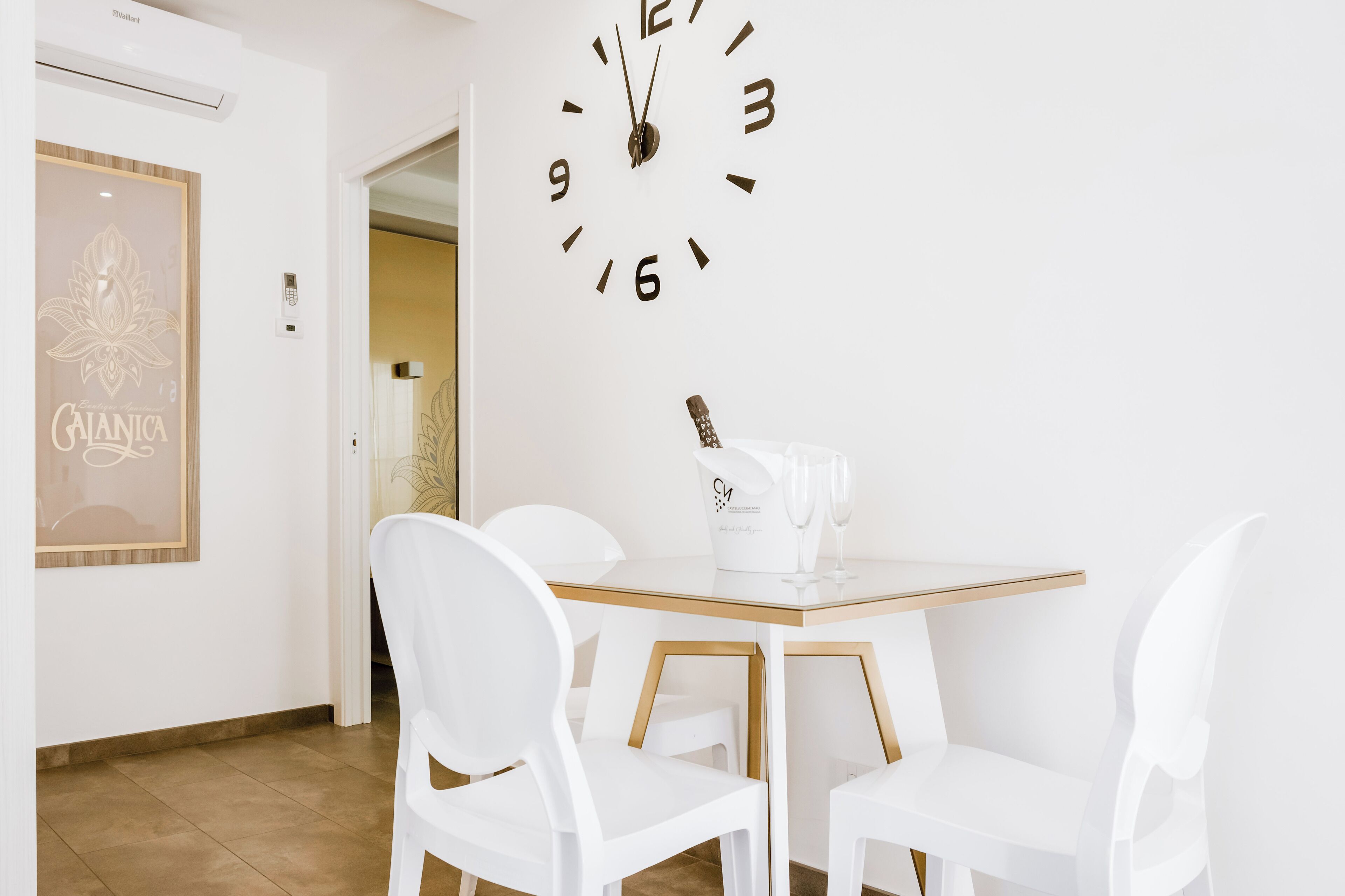 A modern dining area with a white table, four white chairs, and a wall clock.