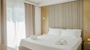 A hotel room with a large bed, a nightstand, a bedside table, and a window with curtains. - Hotiday Apartments Cefalù (Cefalù)