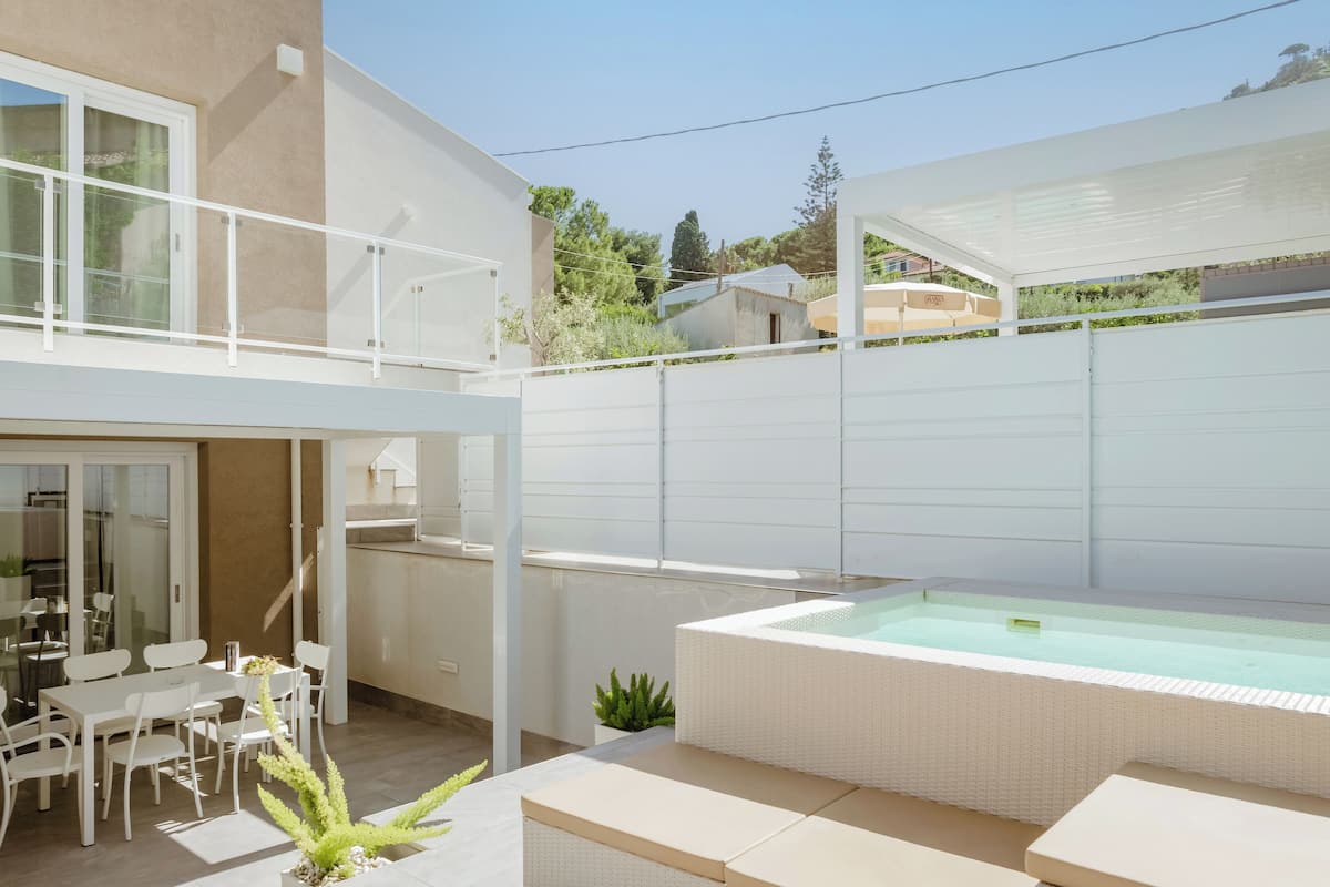 Eine moderne Außenpatio mit Whirlpool, einem Essbereich mit weißem Mobiliar und einer überdachten Sitzgruppe.