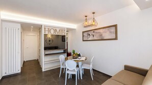 A modern living room with a dining area, a sofa, a chandelier, and a clock. - Hotiday Apartments Cefalù (Cefalù)