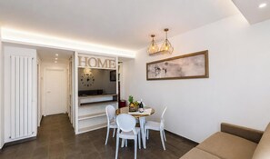 A modern living room with a sofa, a dining table with chairs, a clock, and a painting on the wall. - Hotiday Apartments Cefalù (Cefalù)