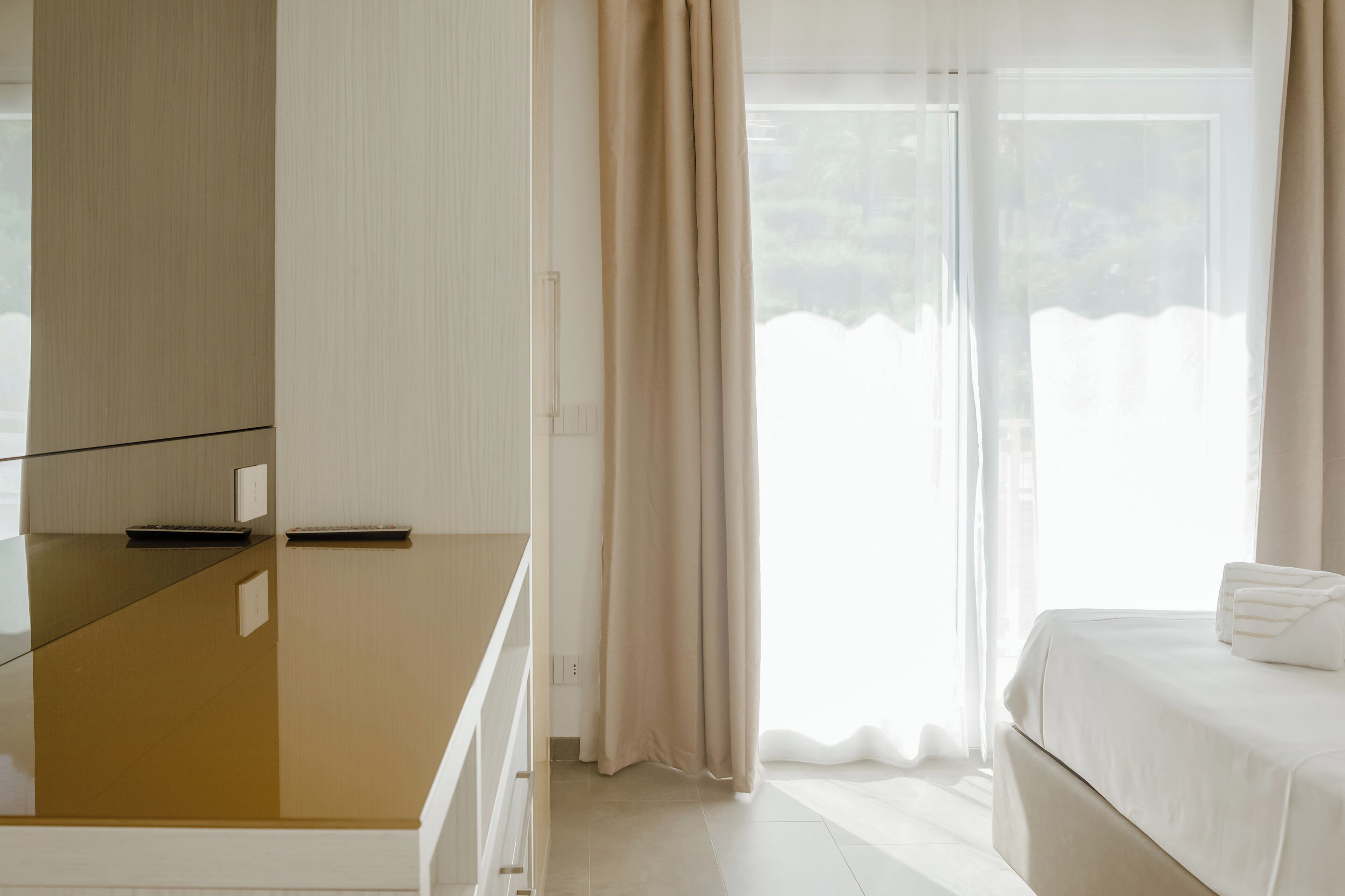 A hotel room with a bed, a desk, and a window with curtains.