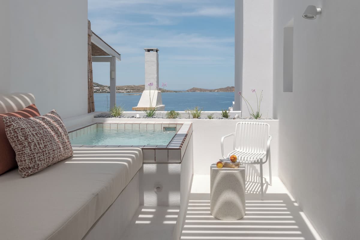 A modern outdoor seating area with a pool, white furniture, and a view of the sea.
