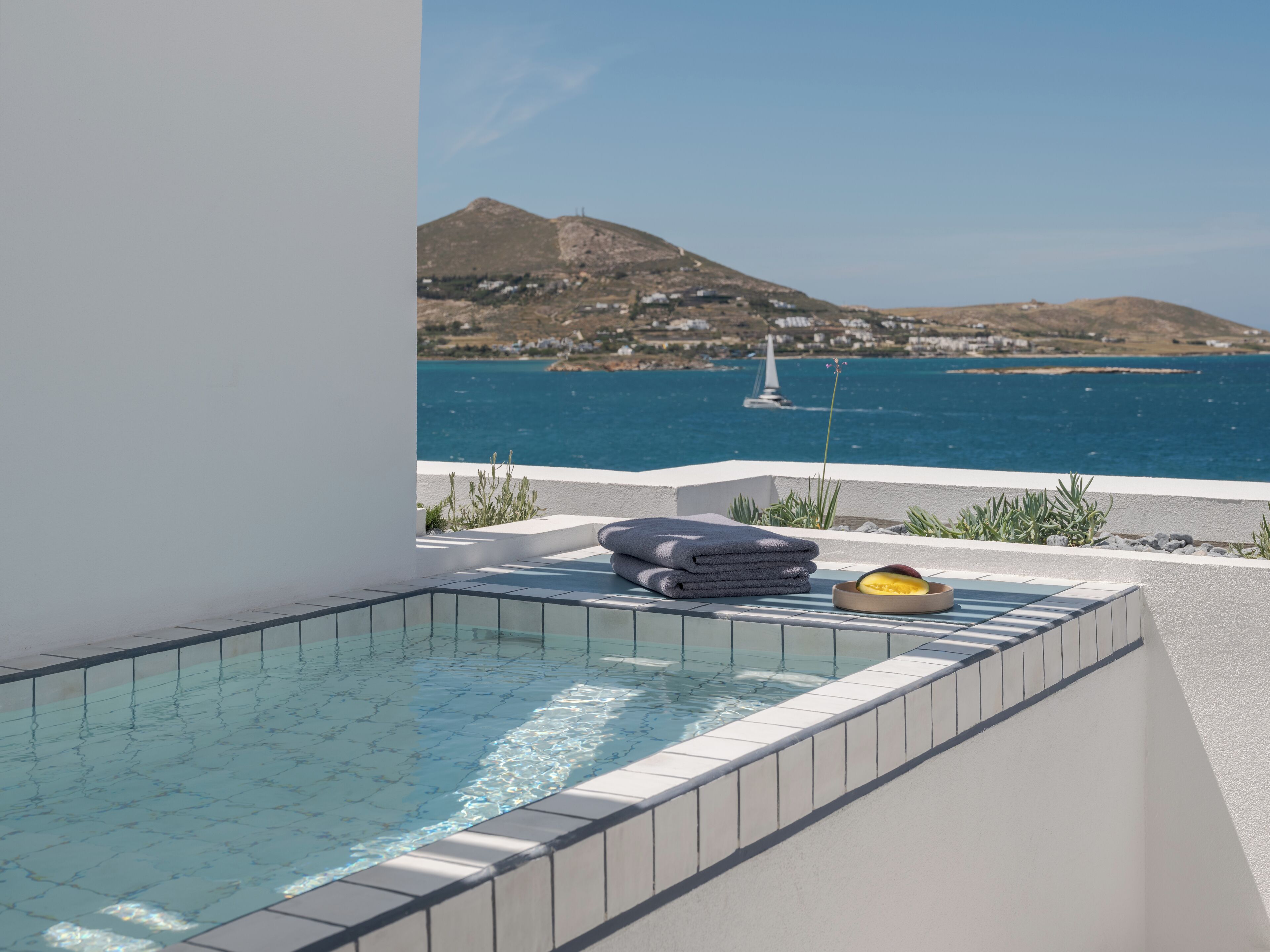 A pool with a clear view of the sea and a sailboat in the distance.