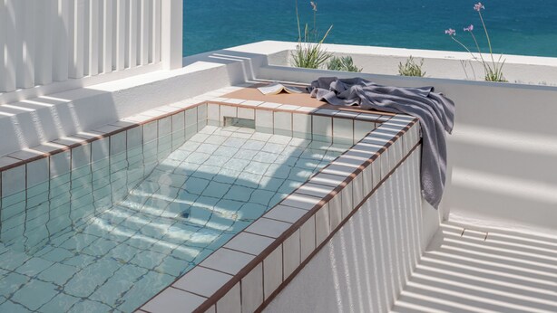 A sunlit outdoor swimming pool with a clear view of the sea and hills in the background. - Aegean Colors Paros (Paros)