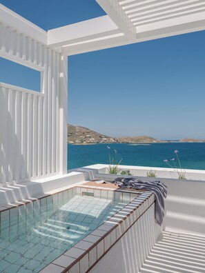 A sunlit outdoor swimming pool with a clear view of the sea and hills in the background. - Aegean Colors Paros (Paros)