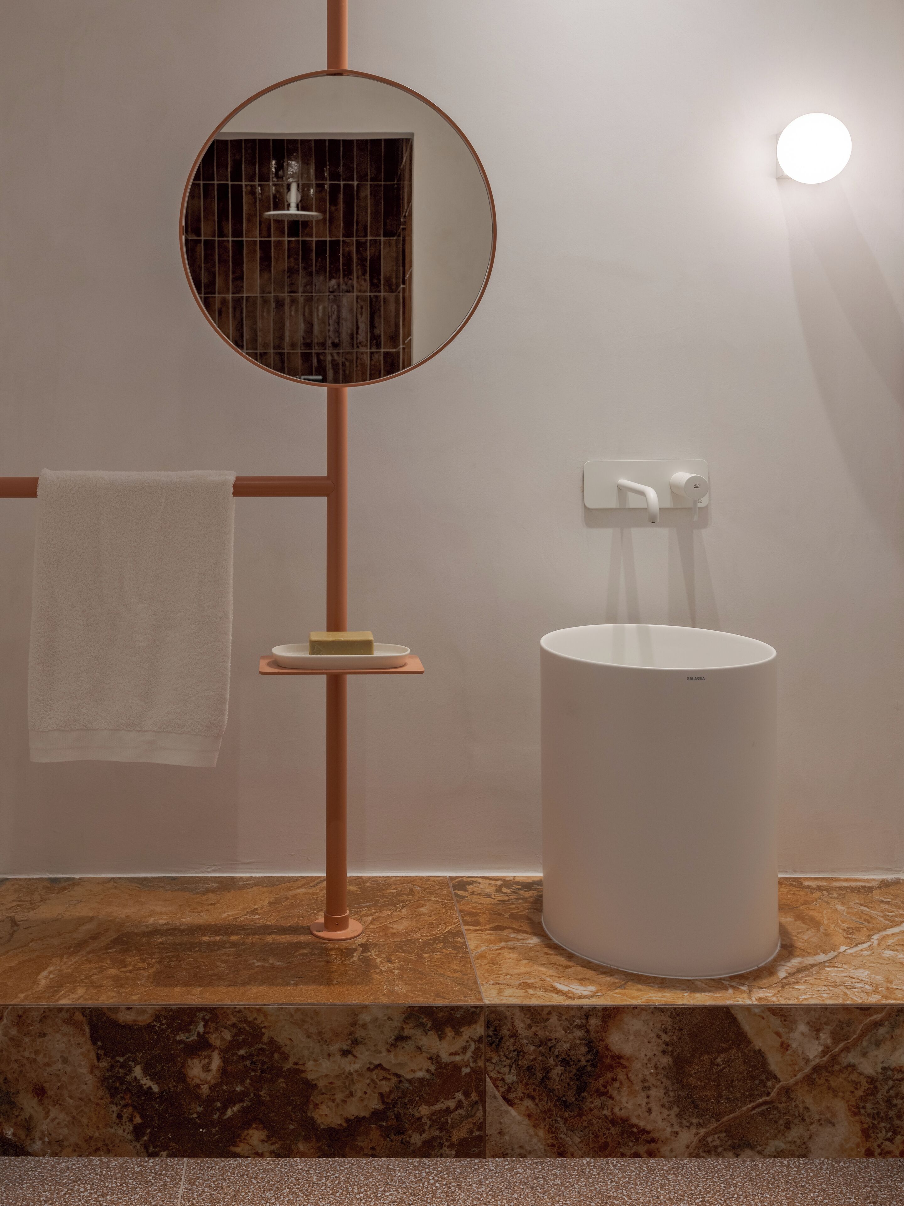 Un baño con un espejo redondo, toallero, lavamanos y jabonera.