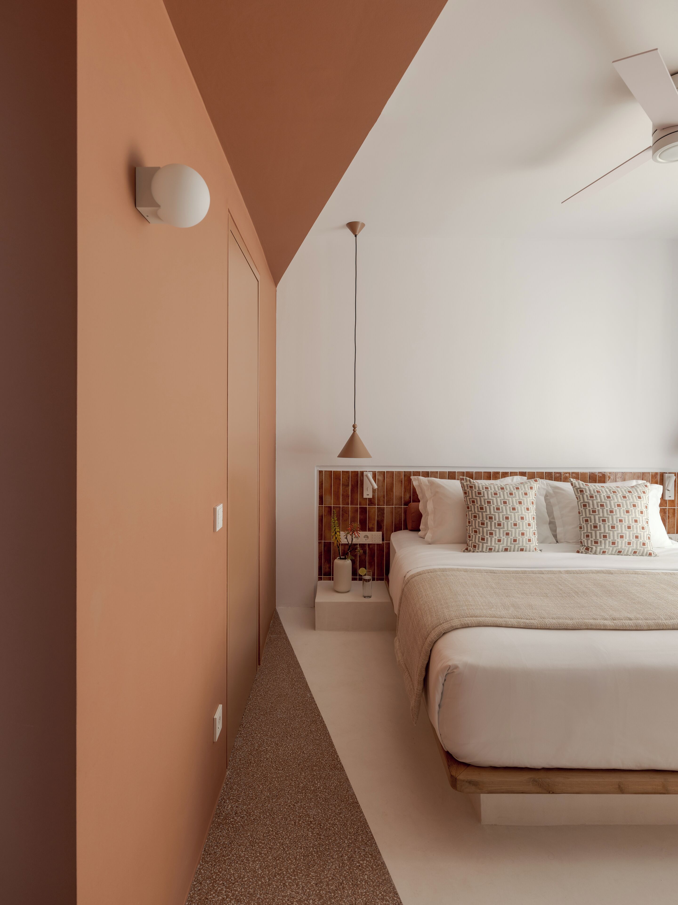 Une chambre moderne avec un grand lit, une table de chevet, une lampe fixée au mur et un ventilateur de plafond.