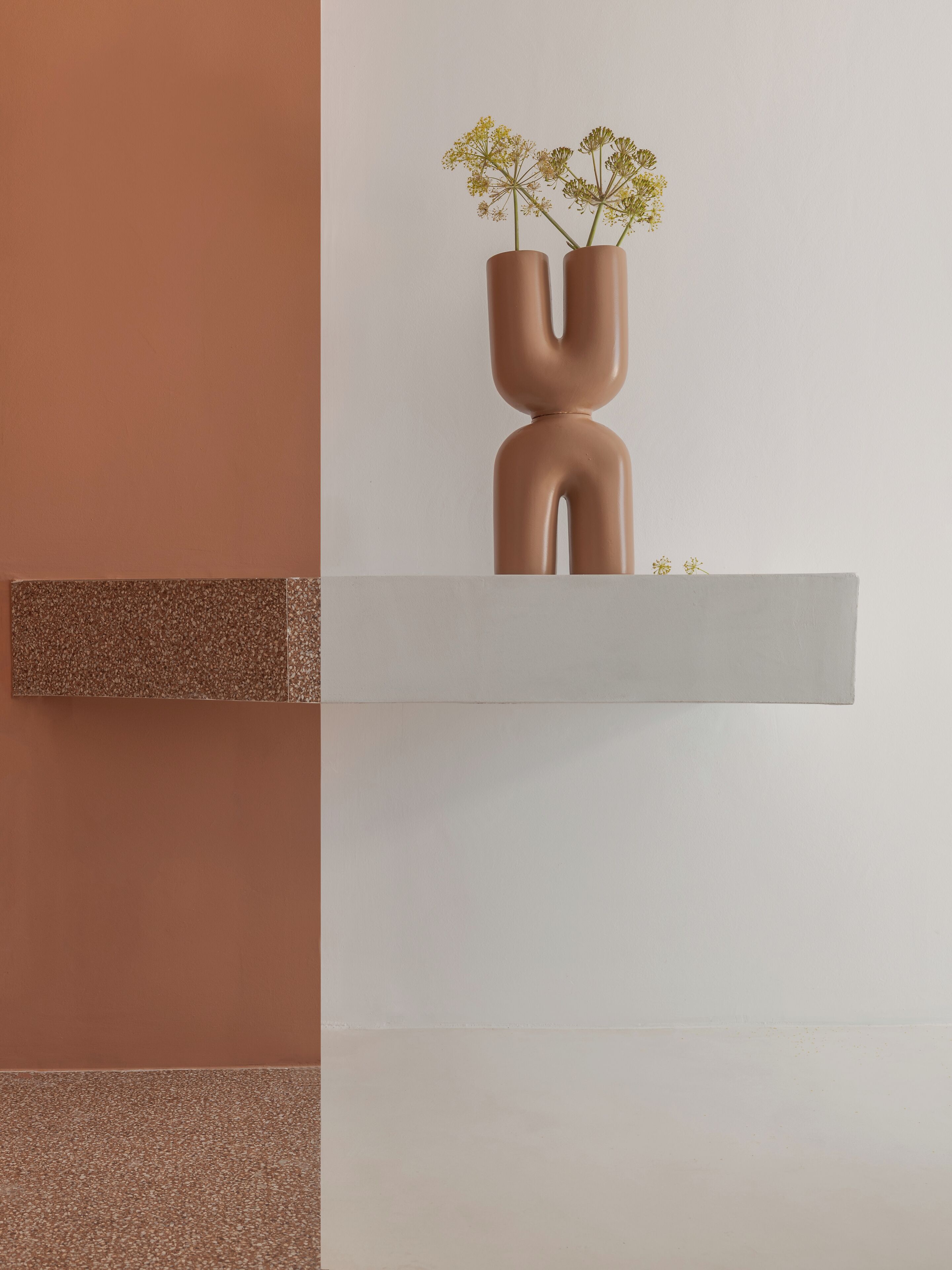 Een minimalistische plank met twee abstracte vazen gevuld met gele bloemen.