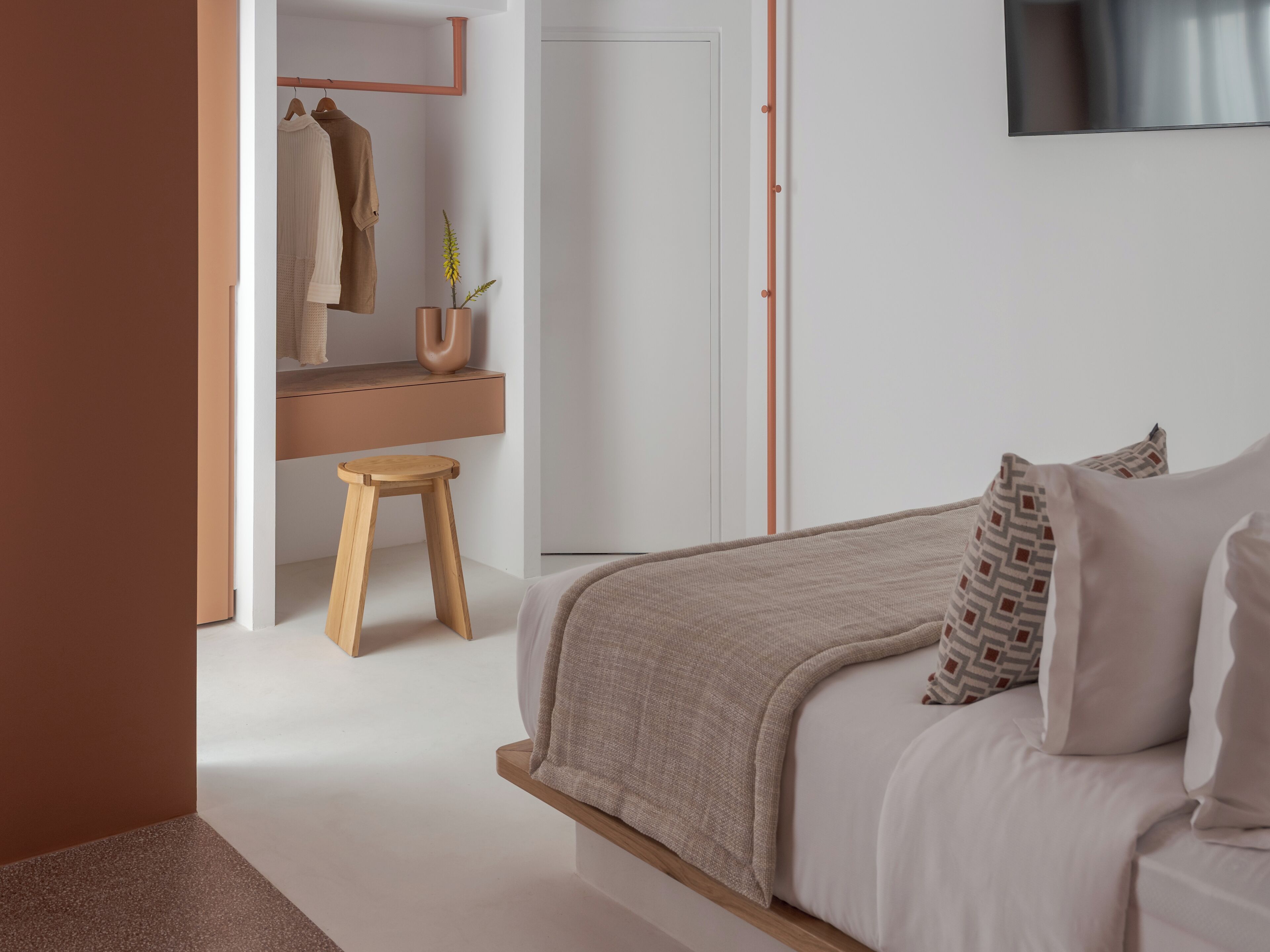 A bedroom with a bed, a wooden stool, a mirror, and a potted plant.