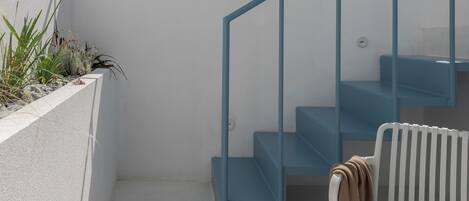 A modern outdoor seating area with a white bench, a small round table with a drink and fruit, and a blue staircase.