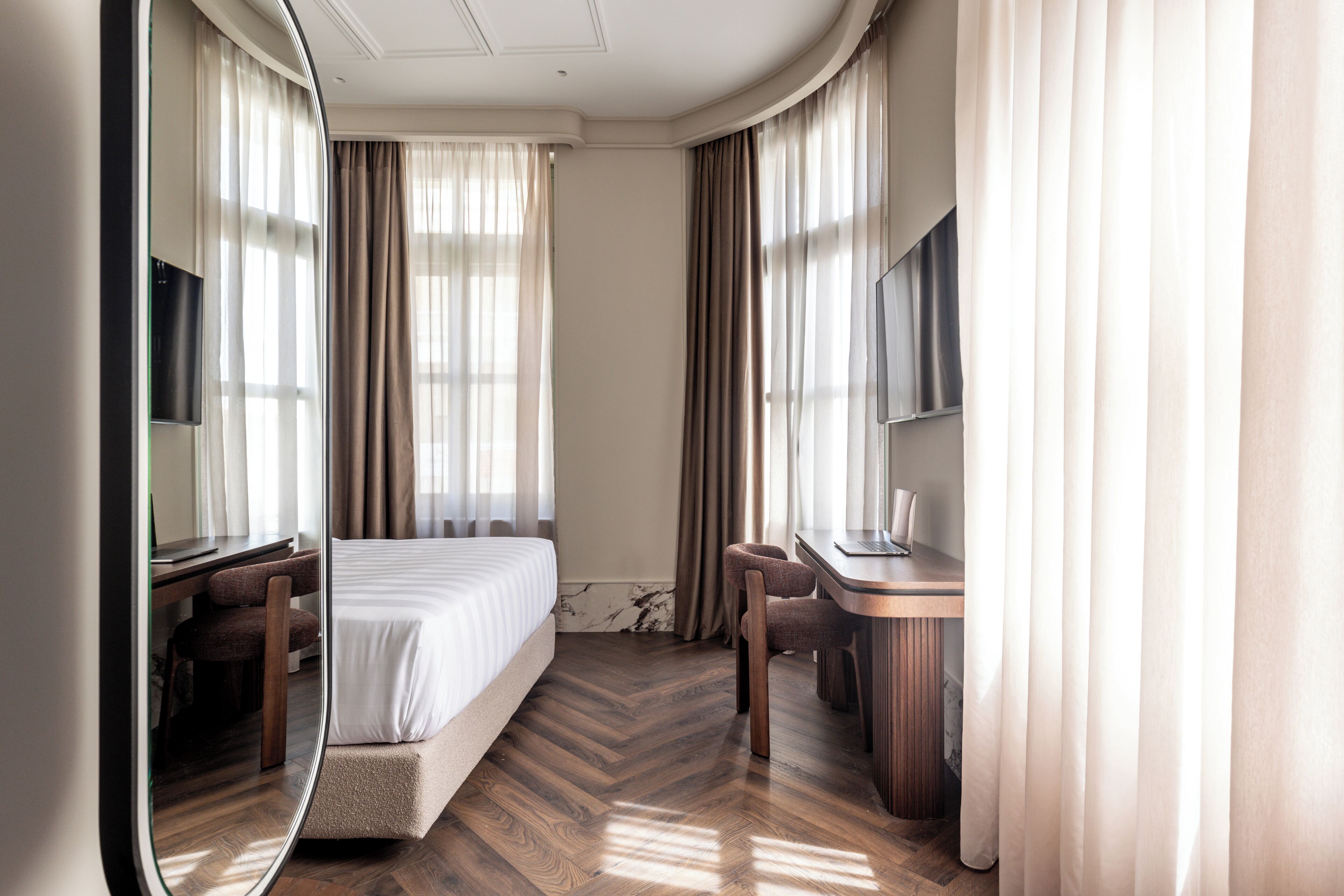 A hotel room with a bed, a desk, a chair, a TV, and a large mirror.