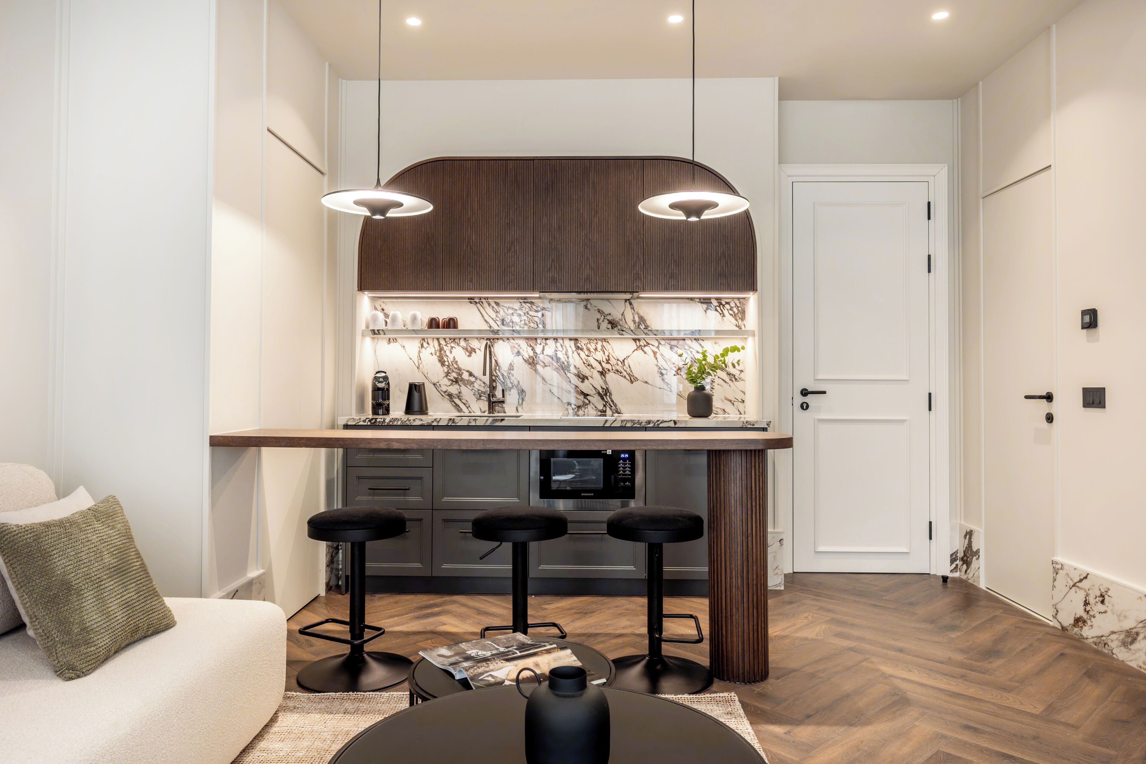 A modern kitchen with a marble countertop, black bar stools, and pendant lighting.