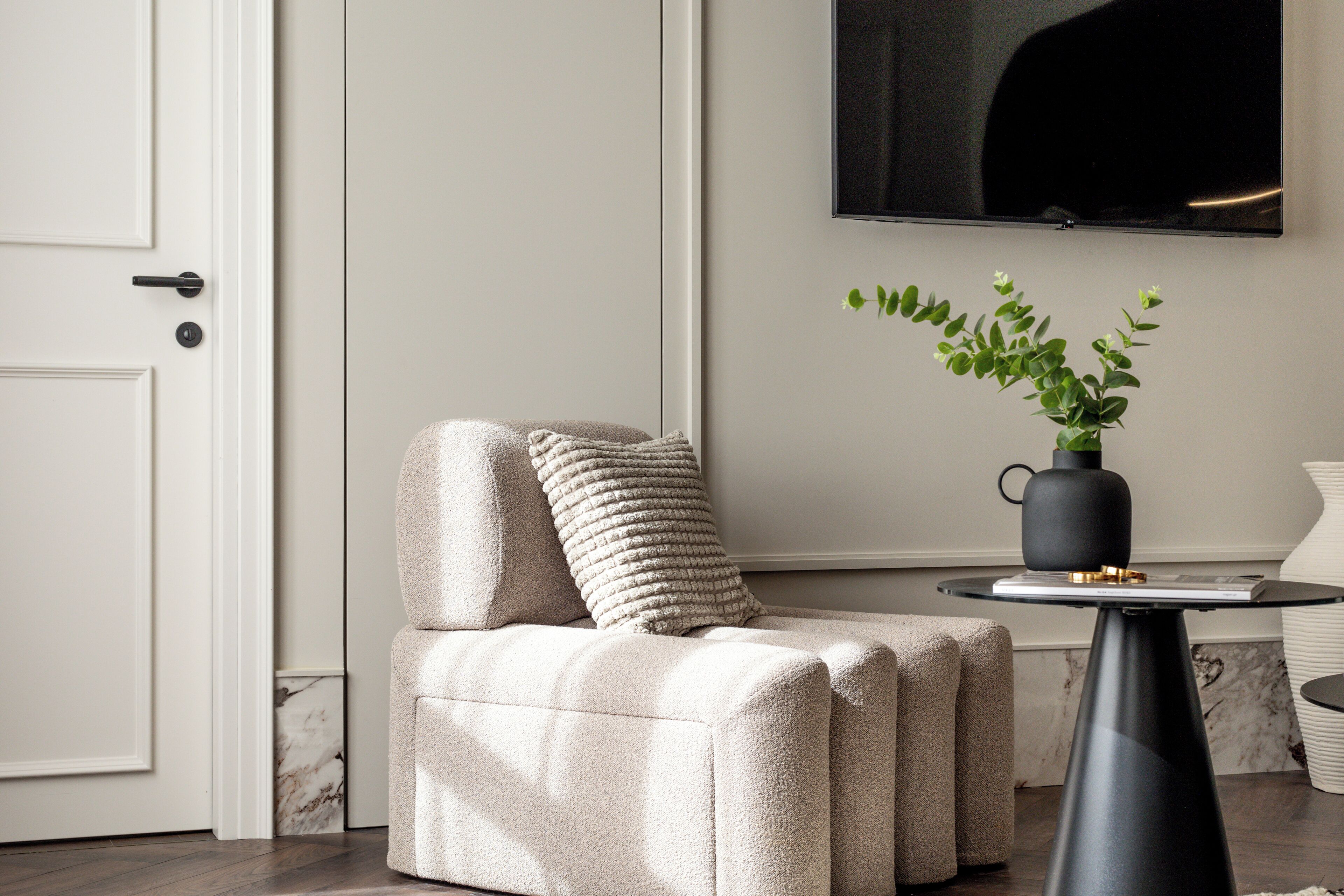 A modern living room with a beige sofa, a small round table, and a potted plant.