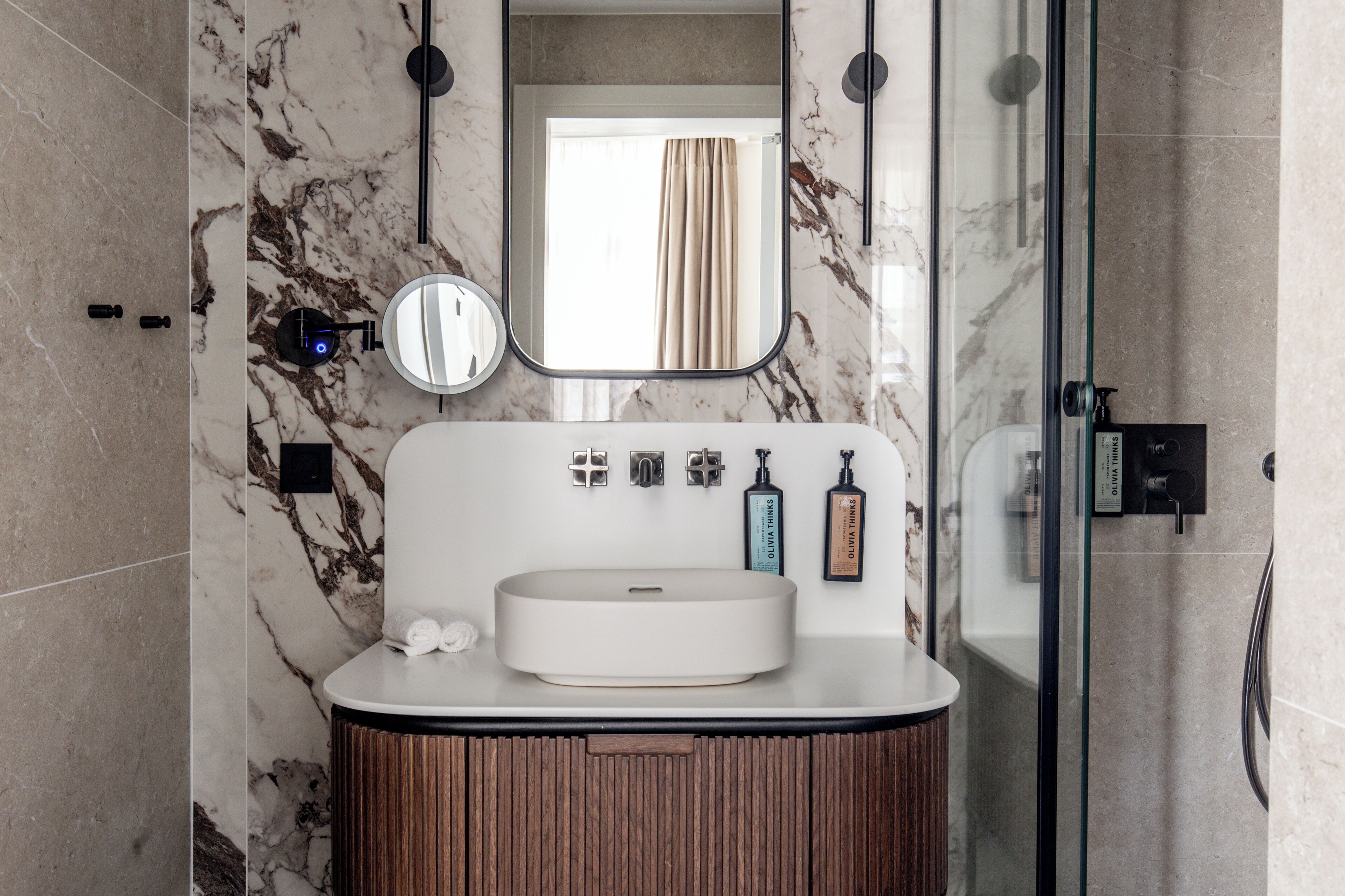 Une salle de bain moderne avec un pare-baignoire en marbre, un lavabo rond, un meuble-lavabo en bois et une cabine de douche en verre.