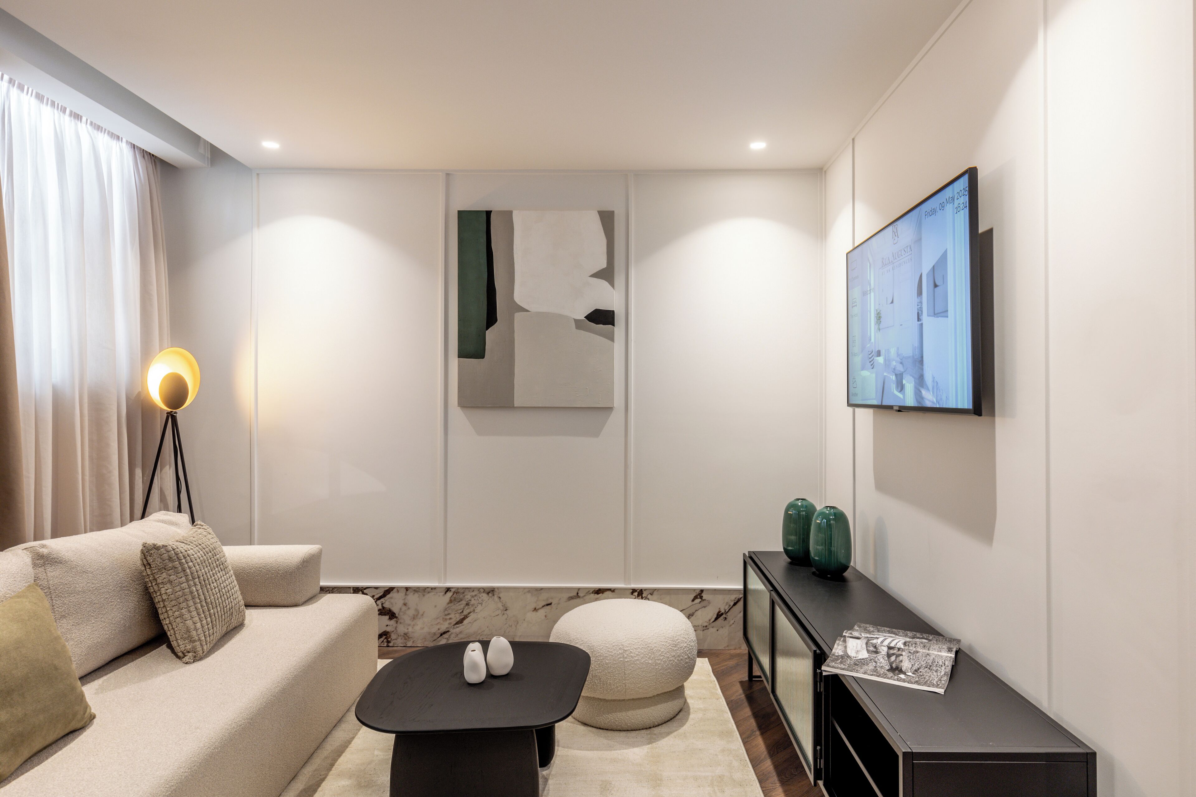 Un salon moderne comprenant un canapé, une table basse, un lampadaire, un tableau, un téléviseur et un buffet agrémenté d’objets décoratifs.