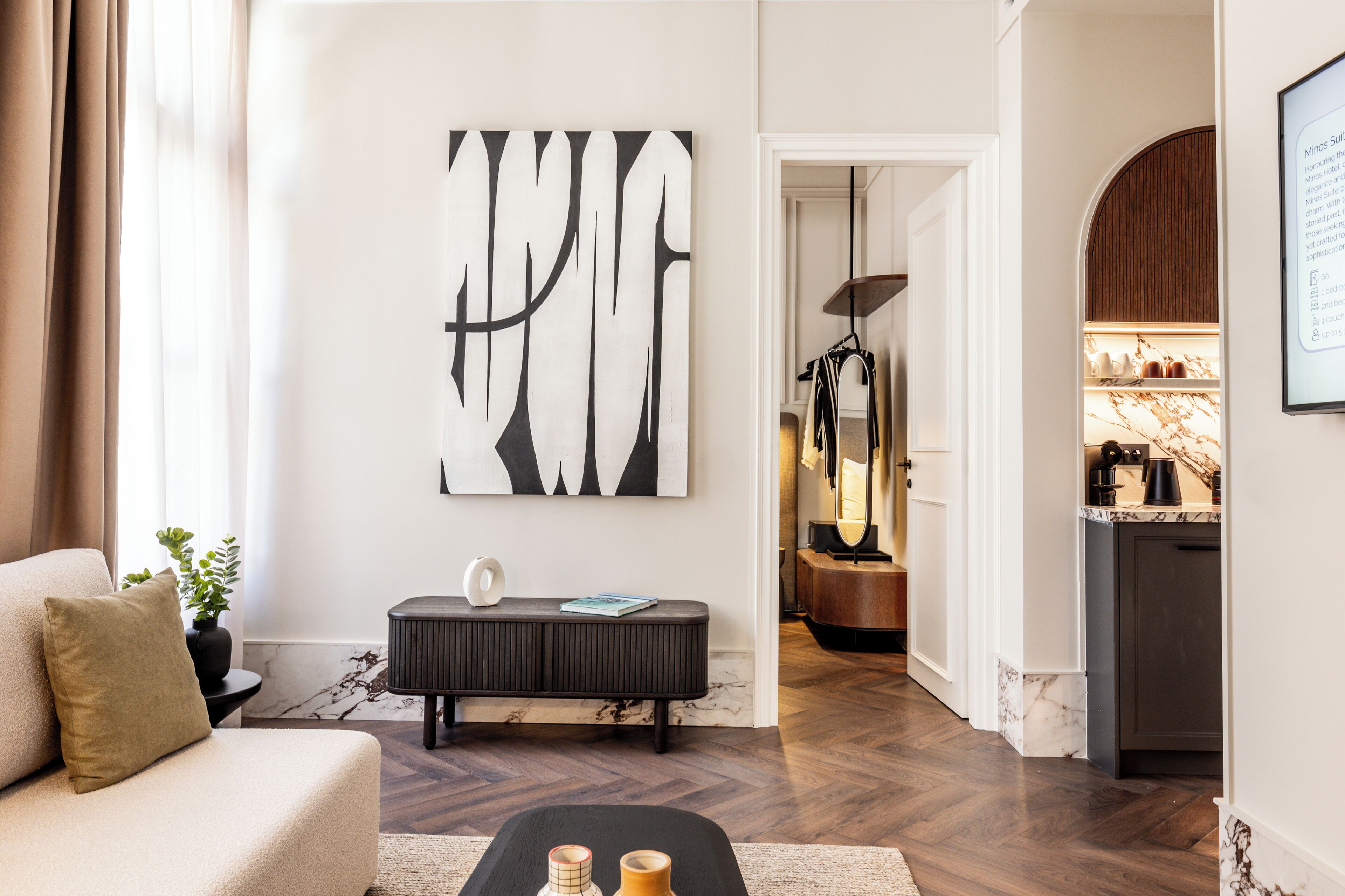 A modern living room with a large abstract painting, a sofa, a console table, and a kitchen area in the background.