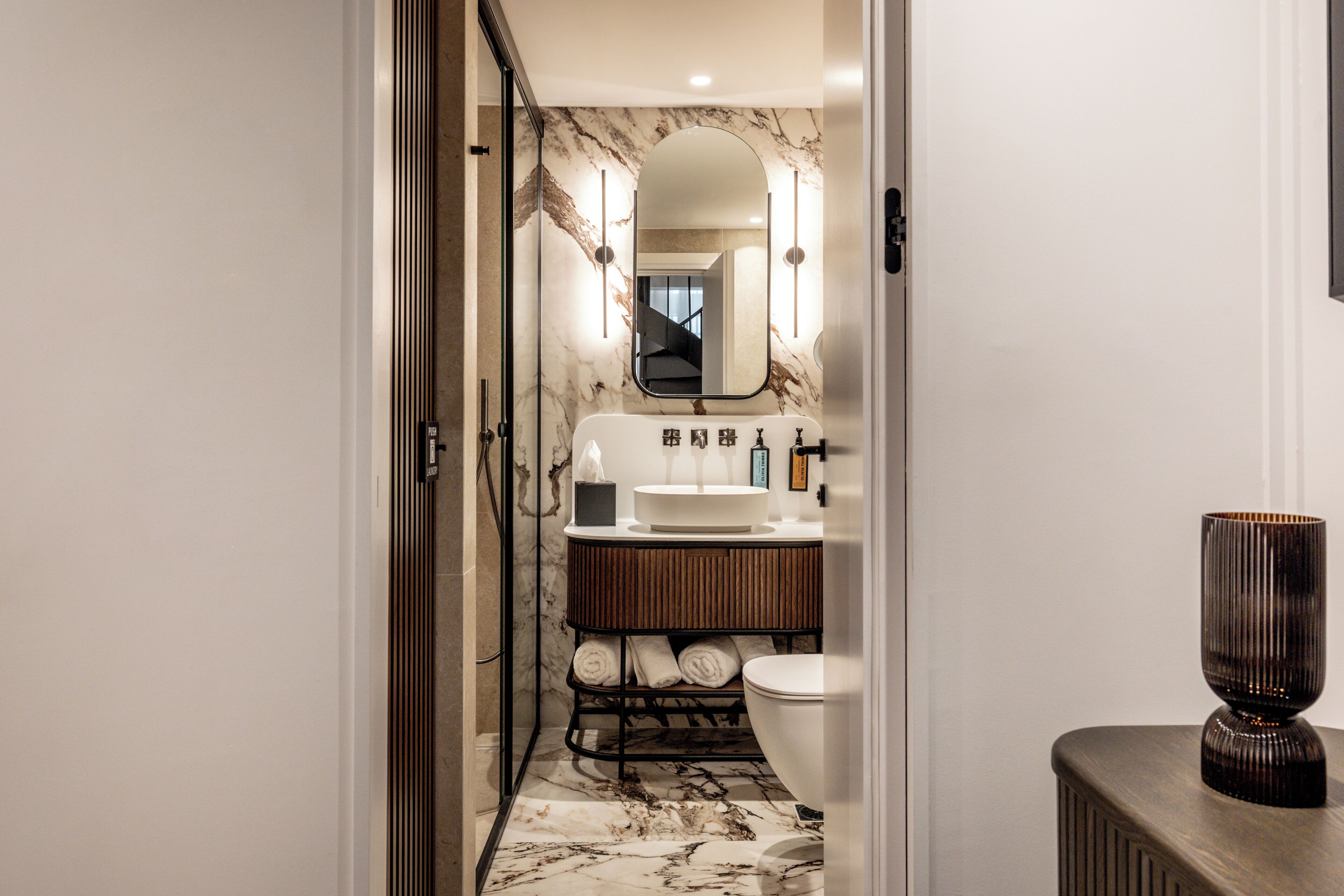 Un baño moderno con suelo de mármol, un lavabo blanco, un inodoro y un espejo con iluminación.