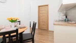 A dining area with a wooden table set for two, a vase of flowers, and a clock on the wall. - TOTU Home Gdańsk Marina Studio Old Town (Gdansk)