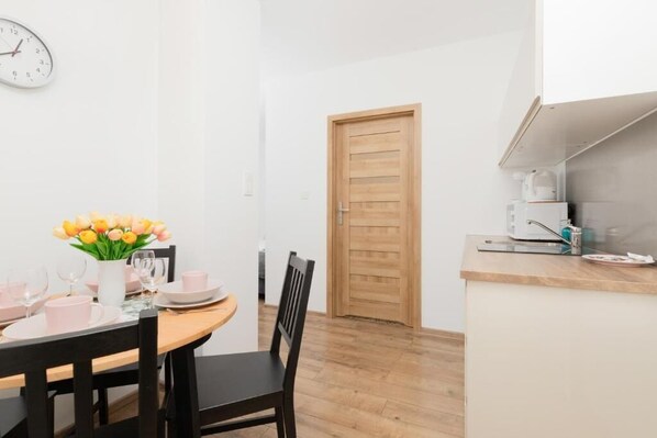 A dining area with a wooden table set for two, a vase of flowers, and a clock on the wall.